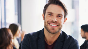 Portrait of a young businessman sitting in an office with his colleagues in the background