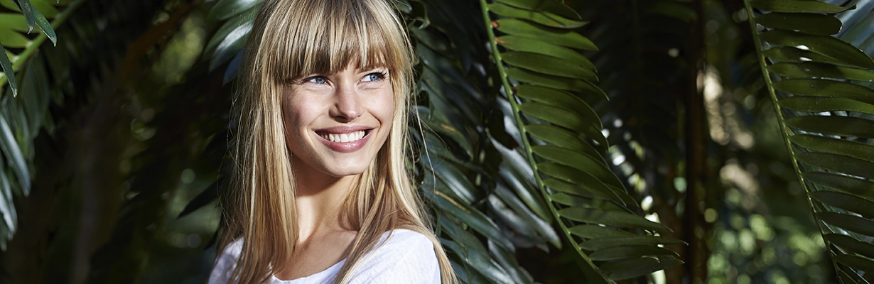 woman smiling in front of tropicla leaves