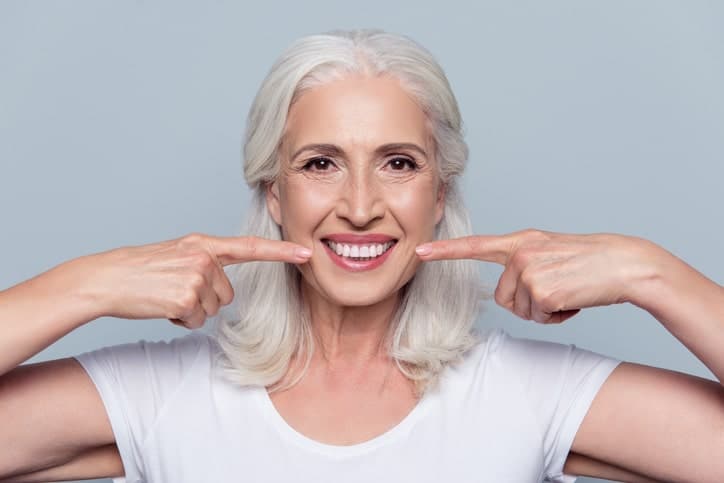older woman happy pointing at her teeth after a smile makeover