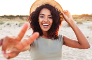 african girl in summer hat showing peace gesture at the beach