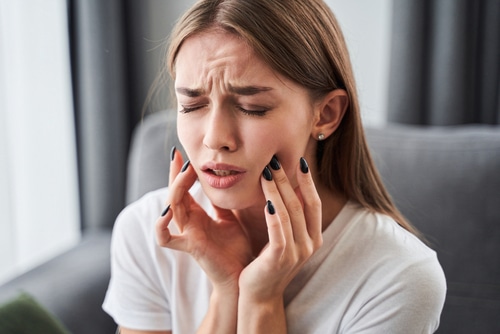 Girl suffering from tooth pain and touching cheek while sitting on couch at home.