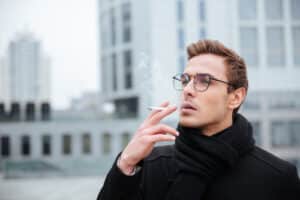 man in glasses and warm clothes smoking cigarette on the street