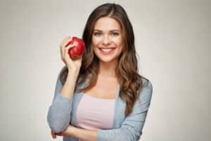 Smiling woman holding an apple, promoting healthy teeth through nutritious food choices