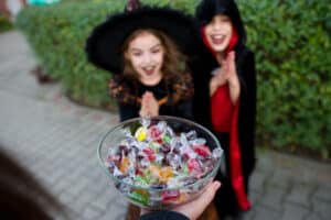 Two little girls trick or treating and a person holding out a bowl of hard candies
