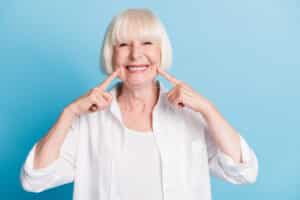 Older woman smiling and pointing to her teeth