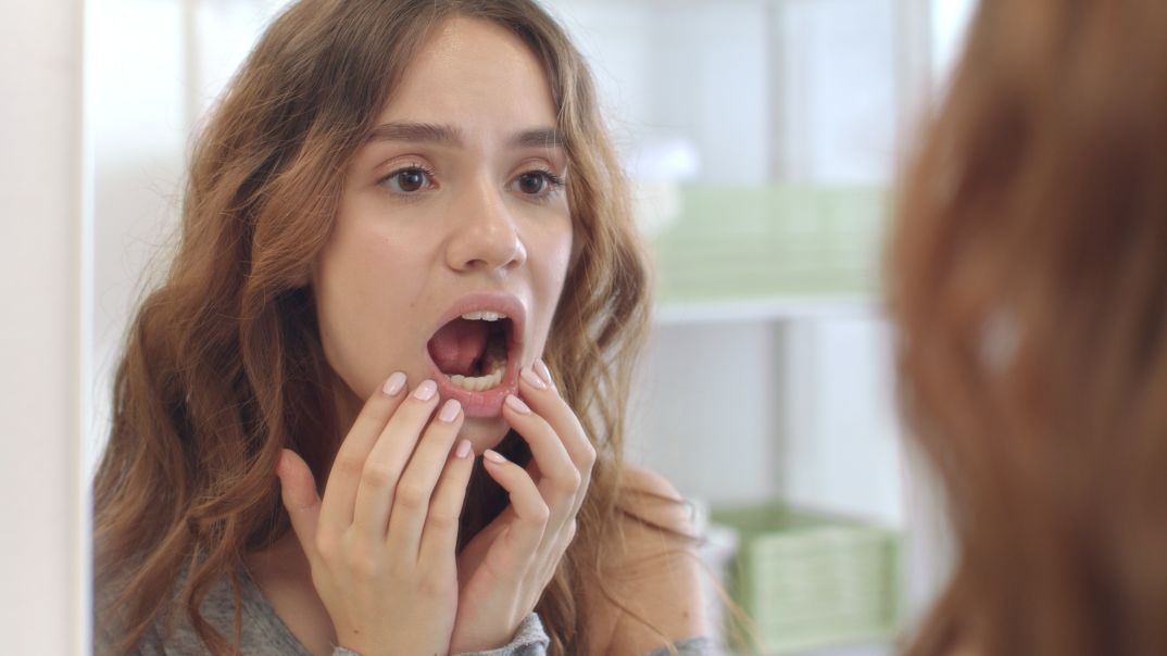 Woman looking in mirror and opening mouth to practice tmj exercisess