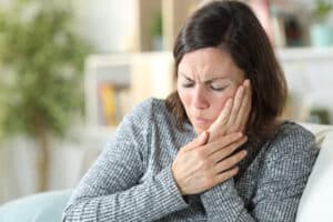 Woman holding her jaw and experiencing severe tooth pain that may be a dental emergency.