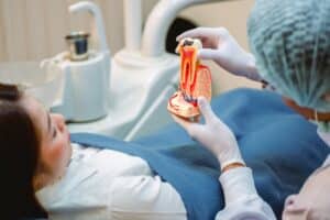 Dentist explaining a tooth model to a patient during an exam for hidden or painless dental problems.