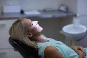 Woman looking relaxed and closing eyes in dental chair after receiving anxiety treatment.